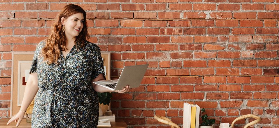plus size girl standing holding laptop in front of brick wall